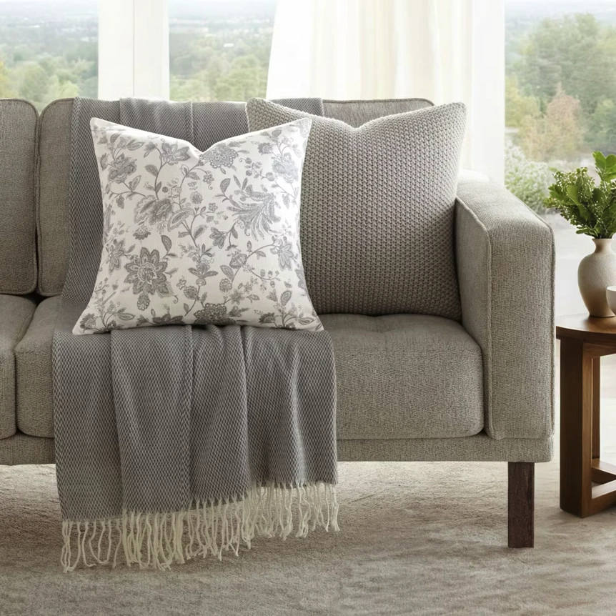 Gray sofa with floral pillow and draped throw blanket in bright living room with windows