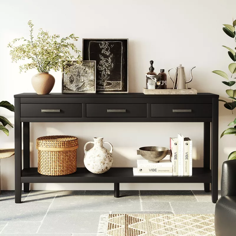 Black console table with three drawers and lower shelf styled with baskets, plants, and decorative items in modern entryway