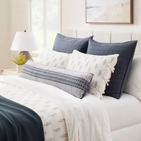 Styled bed with layered white sheets, navy pillows, and gray textured throw blanket in modern bedroom