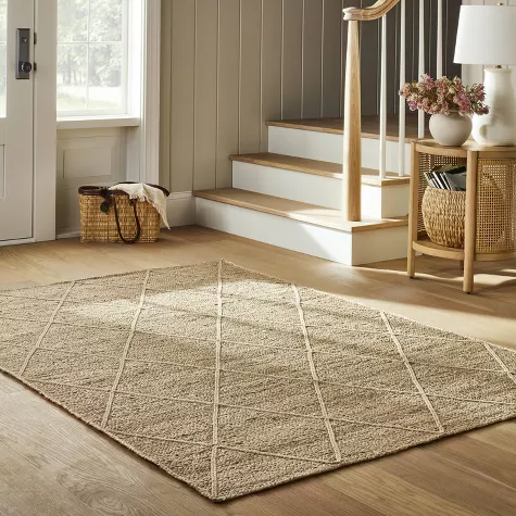 Natural jute area rug with diamond pattern in entryway near wooden staircase and woven baskets