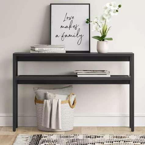 Black two-tier console table with decorative frame, plant, and storage basket in modern entryway setting
