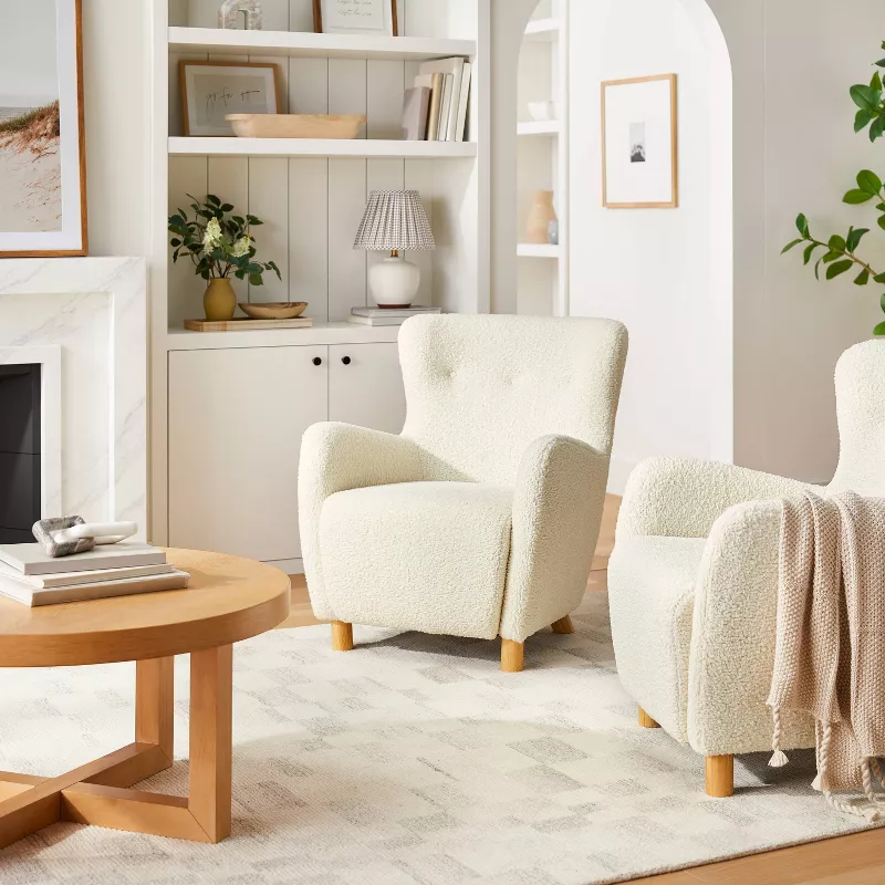 Cream faux shearling wingback accent chair in modern living room with white bookshelf and round wood coffee table