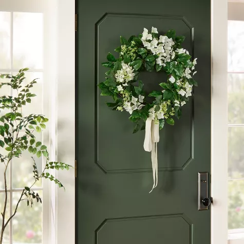 White and green floral wreath with ribbon hanging on dark green front door