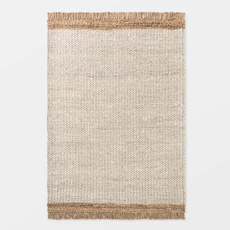 Rectangular jute and wool area rug with natural beige center and tan jute border fringe on white background