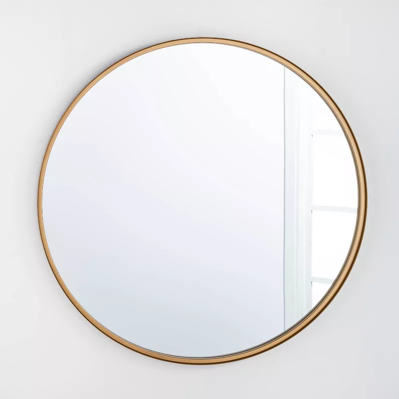 34 inch round decorative wall mirror with thin brass metal frame on white wall