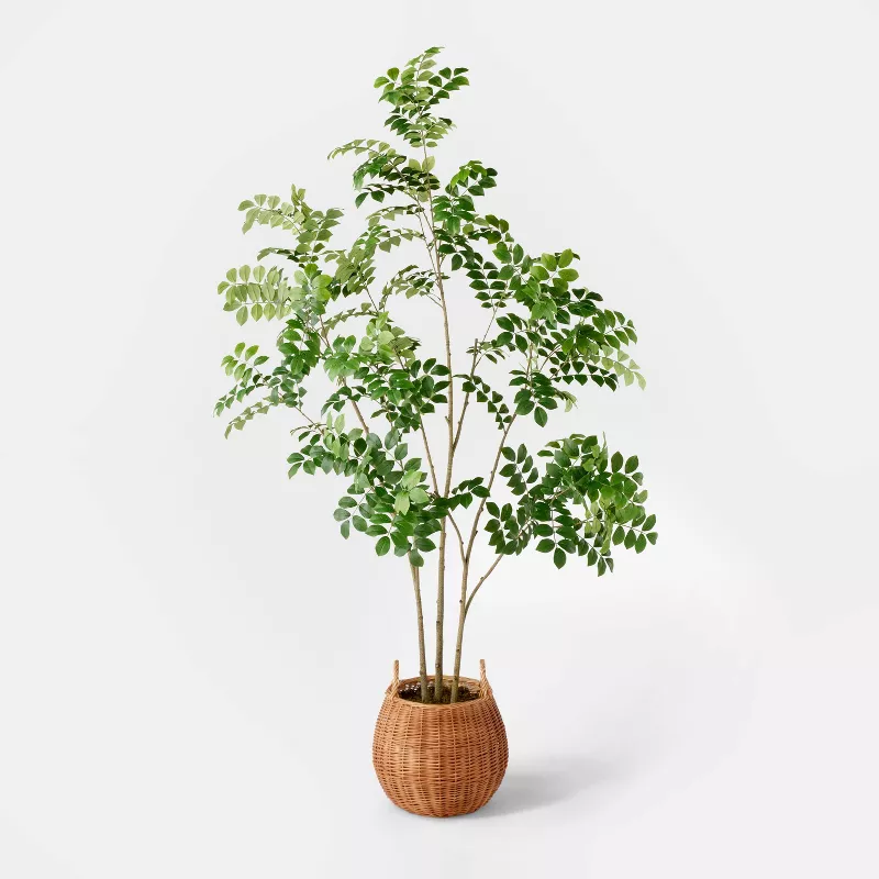 Tall artificial fern plant with delicate green leaves in woven basket planter against white background