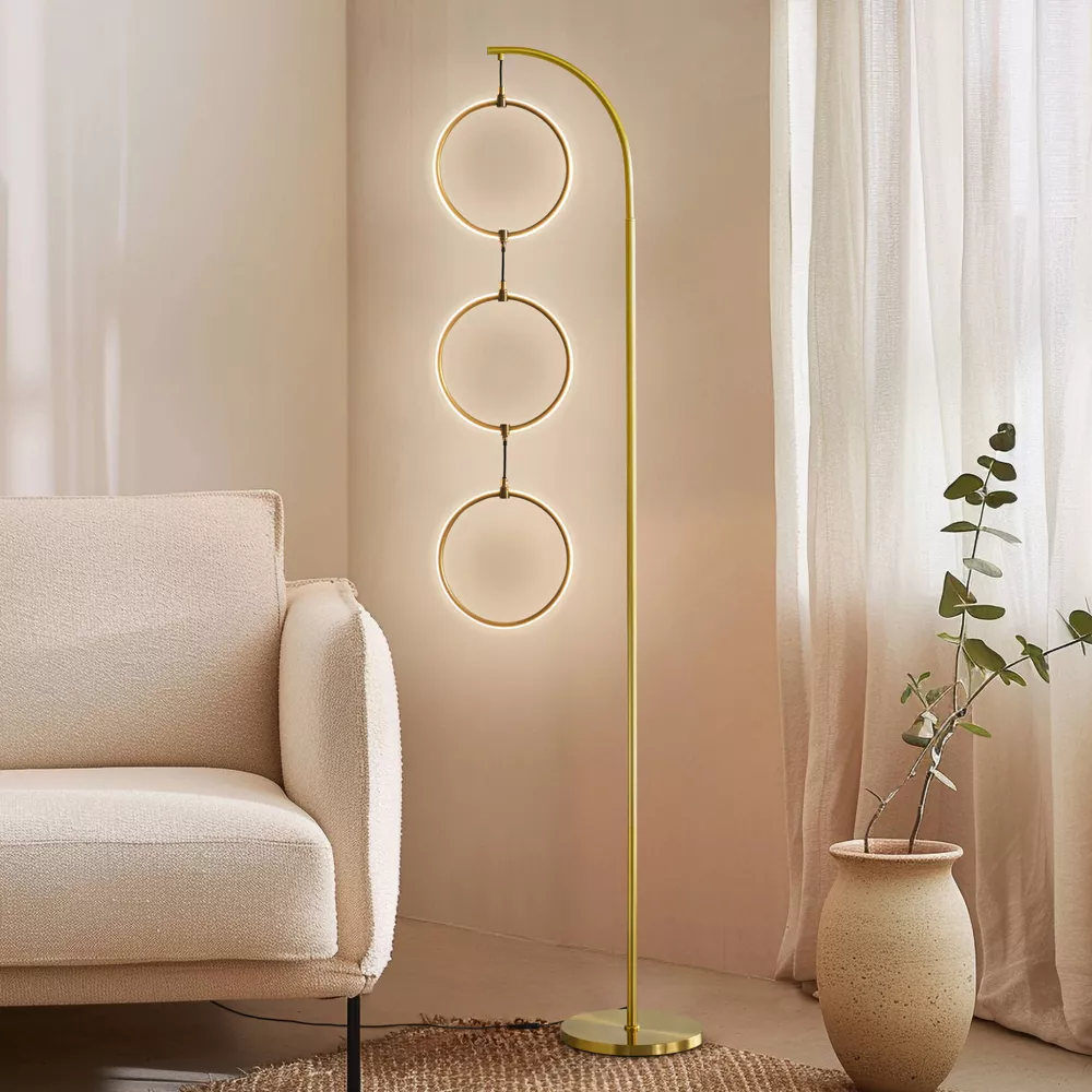 Modern gold floor lamp with three circular rings beside beige sofa in minimalist living room