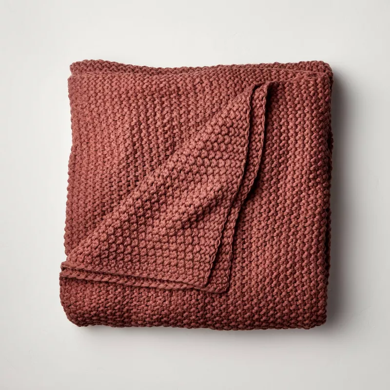 Chunky knit bed blanket in terracotta rust color folded on neutral background