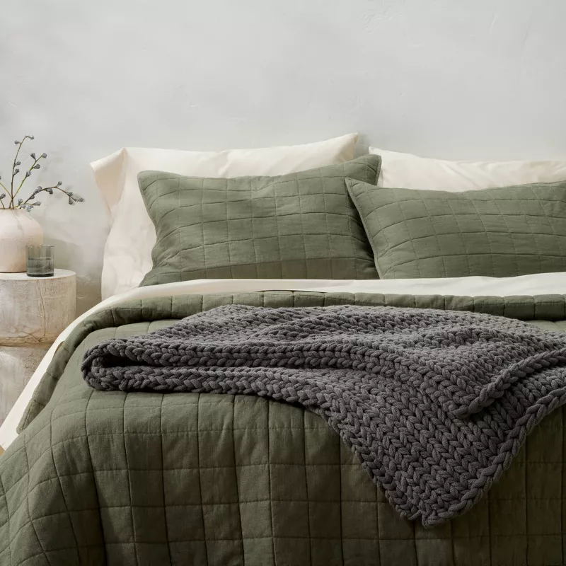 Green quilted bedding set with chunky knit gray throw blanket and decorative pillows on modern bed