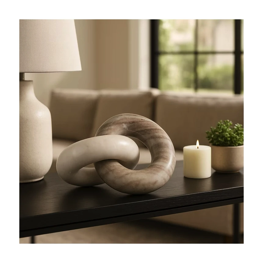 Modern chain link sculpture on black console table with candle and lamp in neutral living room