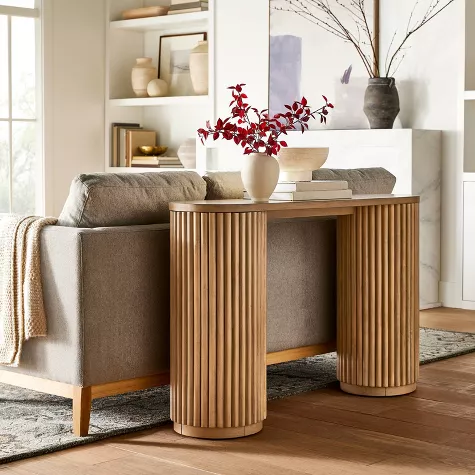 Modern wooden console table with fluted cylindrical legs behind beige sofa in bright living room entryway