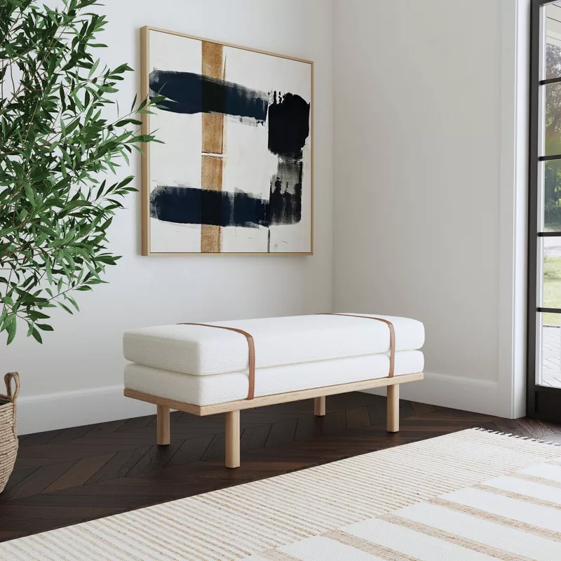 Modern white upholstered bench with wooden frame beneath abstract art and indoor plant in contemporary entryway
