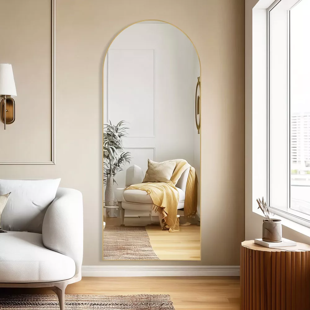 Arched doorway with full-length mirror revealing cozy reading nook with cream chair and warm neutral tones
