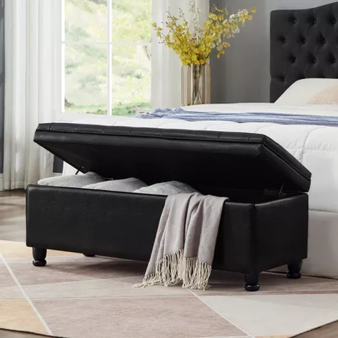 Black tufted storage bench with open lid at foot of bed in modern bedroom with white bedding and yellow flowers