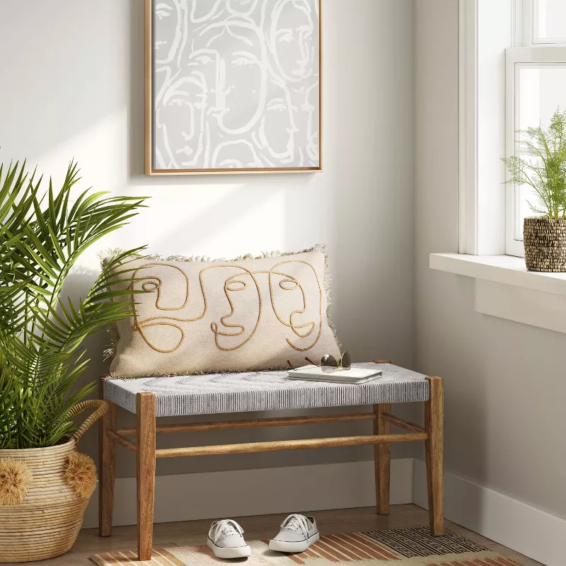 Modern wooden storage bench with white cushion and decorative pillow in minimalist entryway with plants
