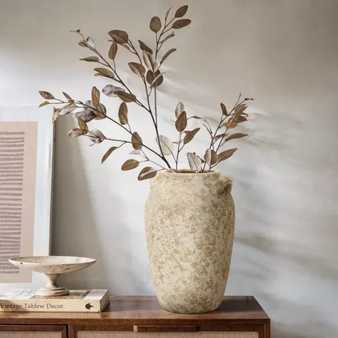Vintage pottery vase with dried brown branches on wooden table against white wall