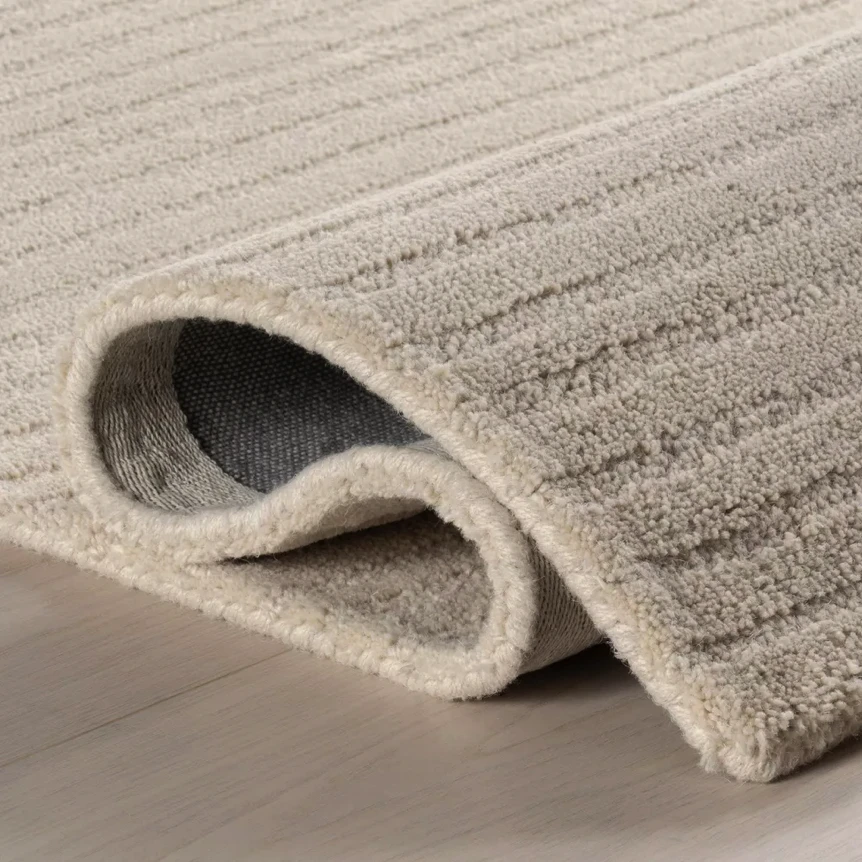 Rolled corner of textured beige area rug showing underside backing and ribbed pattern detail