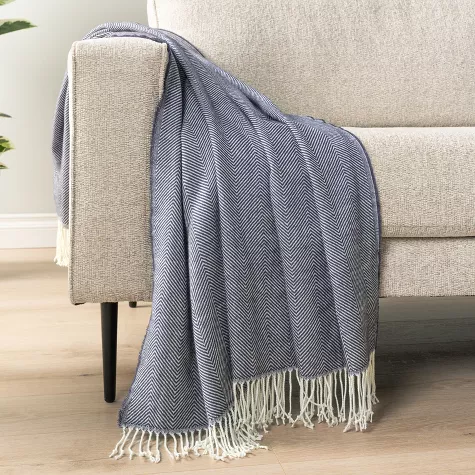 Navy blue knit textured throw blanket with fringe draped over beige couch armrest in living room setting
