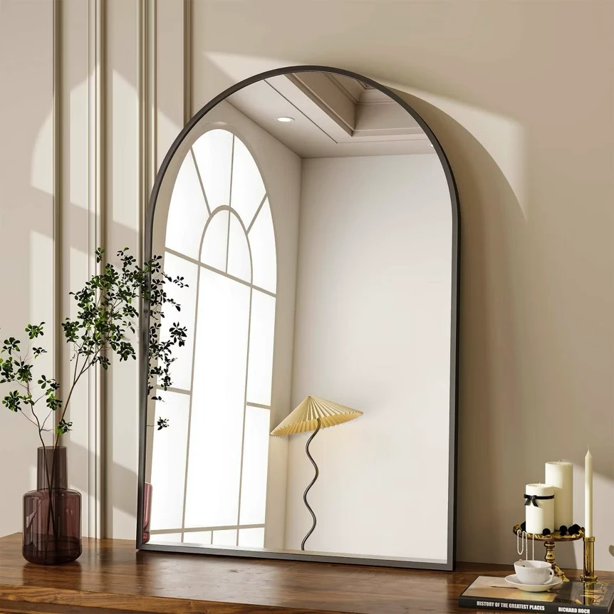 Large arched wall mirror with metal frame reflecting natural light and decor in neutral minimalist interior