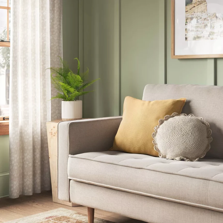 Neutral beige sofa with yellow and gray pillows in bright living room with green walls and natural light