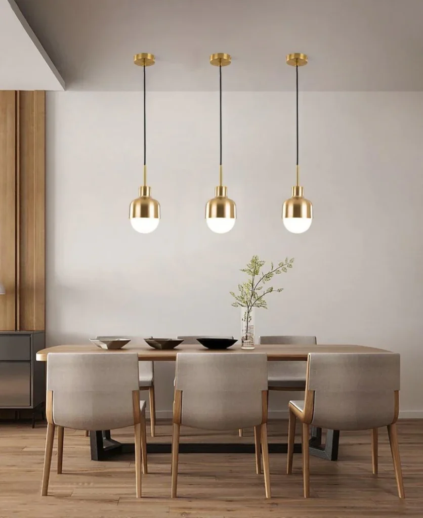 Modern dining room with three gold pendant lights above wooden table and upholstered chairs