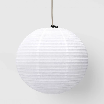 Round white ribbed paper pendant light shade hanging from cord against neutral background