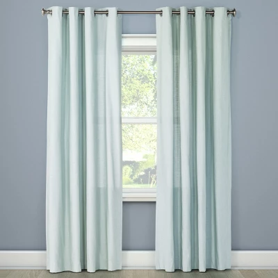 Light filtering aqua curtain panels with grommet top hanging on rod beside window in room with gray walls