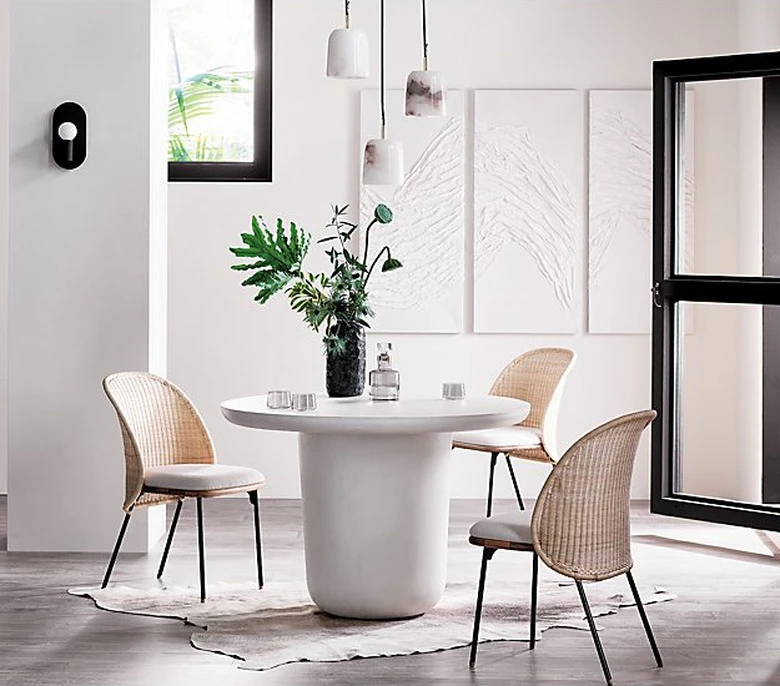 Modern dining room with white round table, woven chairs, and pendant lighting over table with natural light