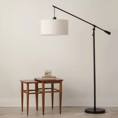 Cantilever floor lamp with white drum shade and bronze finish next to wooden side table