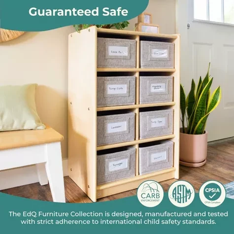 A natural colored wooden cubby storage organizer with eight fabric bins each labeled is placed in a room with a plant and a bench nearby featuring safety certification logos at the bottom 1