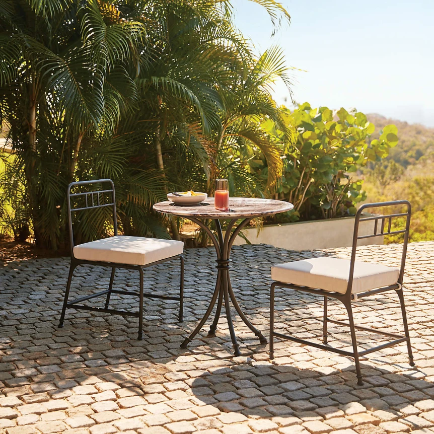 Small bistro patio set with two chairs and round table on cobblestone terrace surrounded by tropical plants