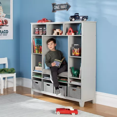 Child sitting in white storage cubby unit with shelves displaying toys and books in blue bedroom