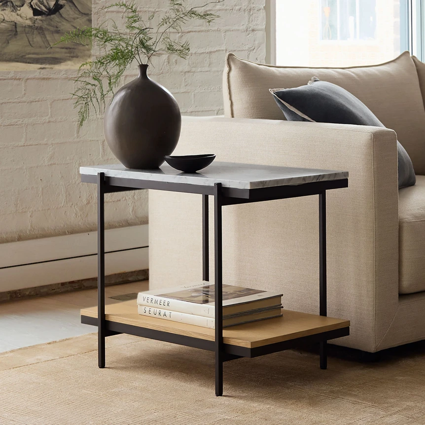 Modern two tier side table with black metal frame and white marble top next to beige sofa in living room
