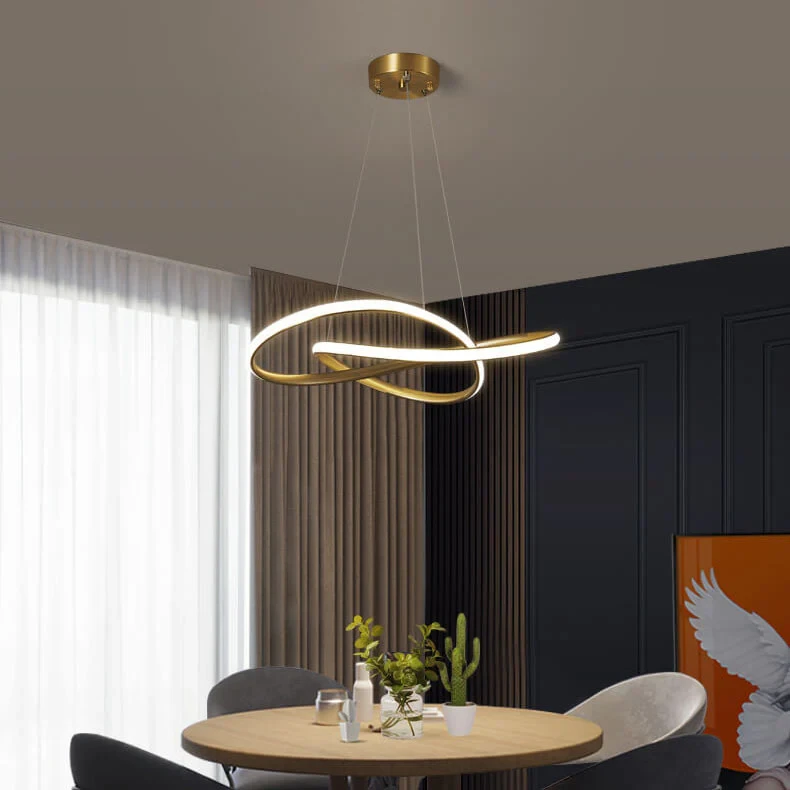 Modern gold pendant light fixture hanging above round wooden dining table with black chairs and dark wall paneling