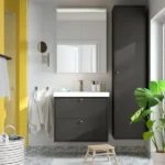 Modern bathroom vanity with dark gray cabinets, white sink, mirror, and tall storage cabinet with green plant