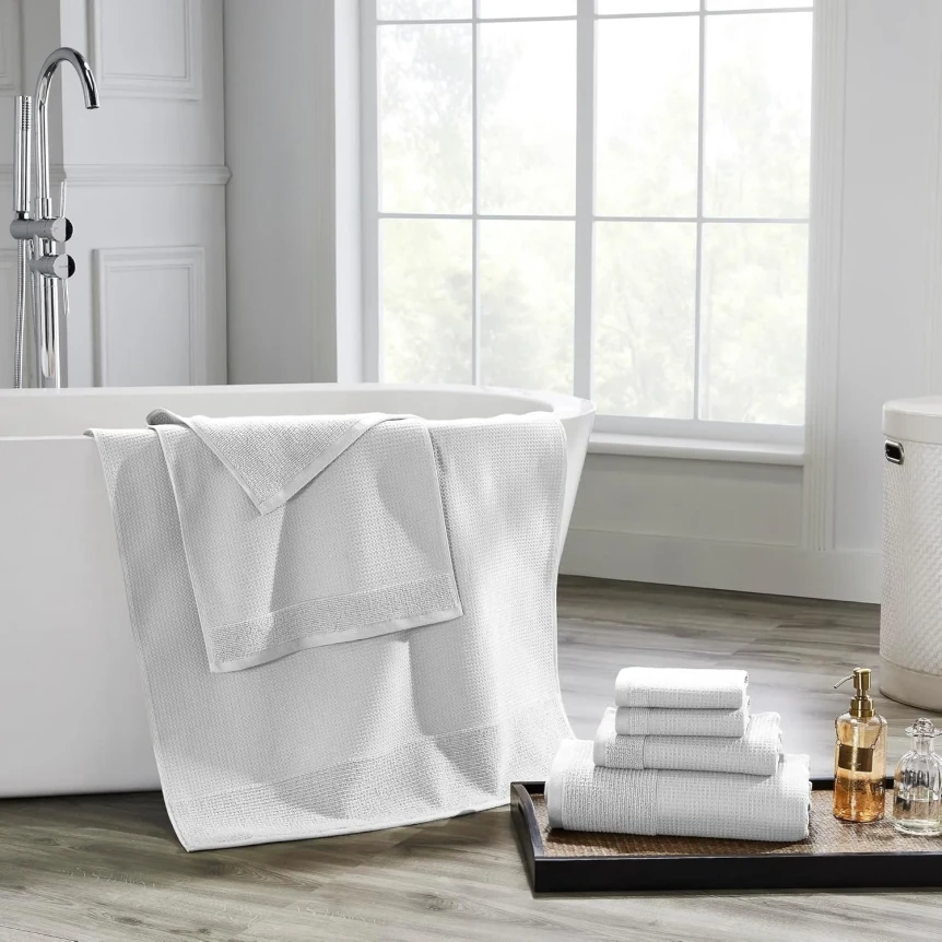 White luxury bath towels displayed on bathtub and stacked on tray with gold soap dispenser in modern bathroom