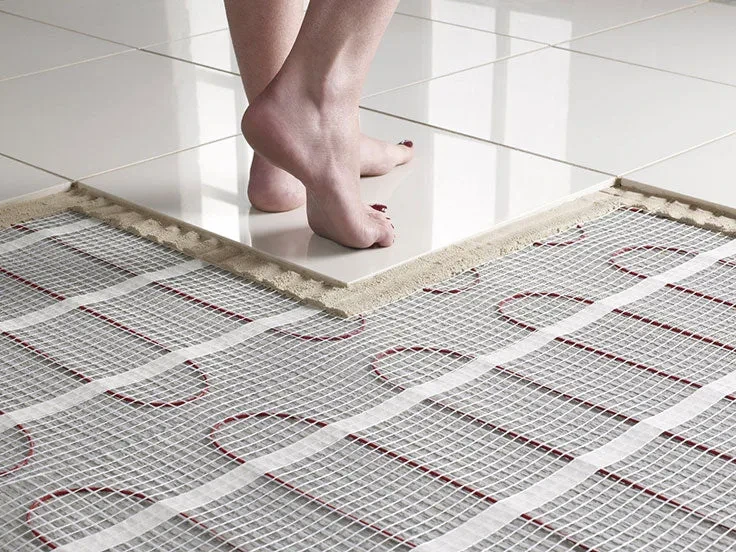 Person standing barefoot on radiant floor heating mat beneath white bathroom tiles during installation