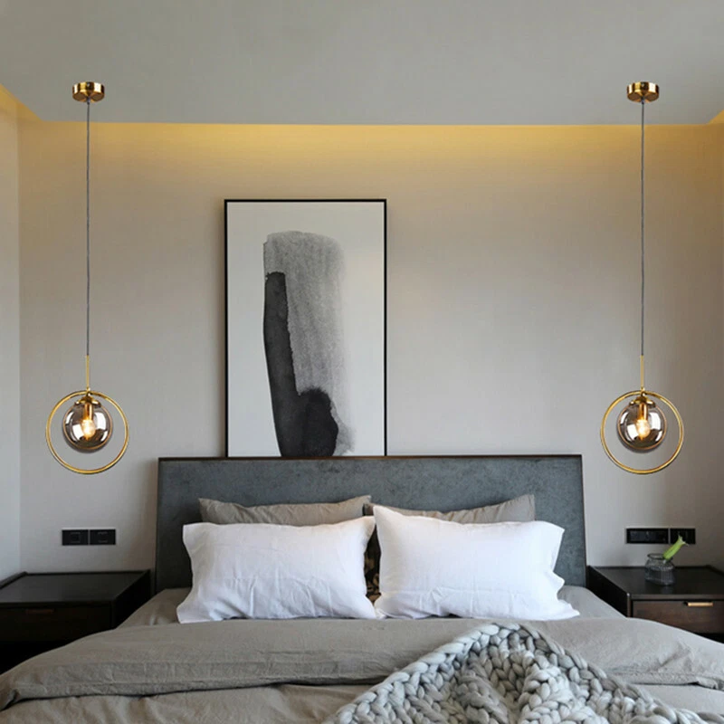 Modern bedroom with golden pendant lights flanking abstract artwork above upholstered headboard and white bedding