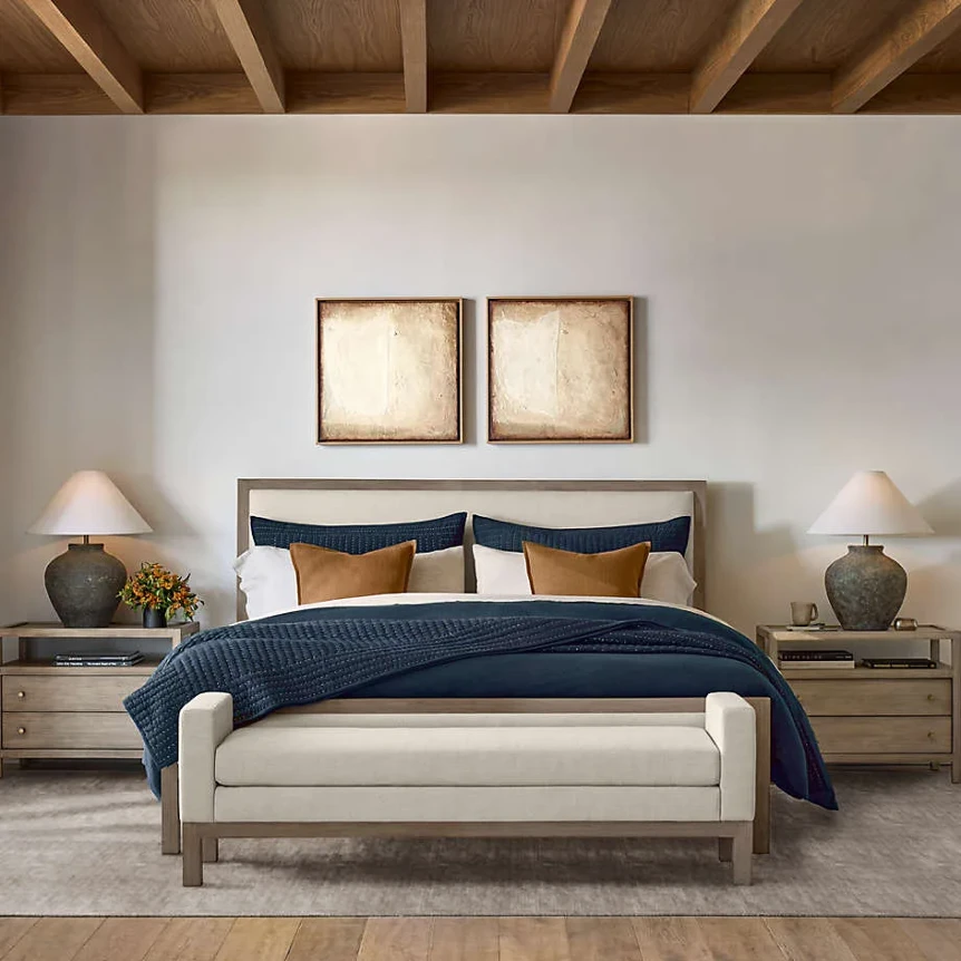 Modern bedroom with wooden bed frame, navy bedding, nightstands, and exposed beam ceiling in neutral tones