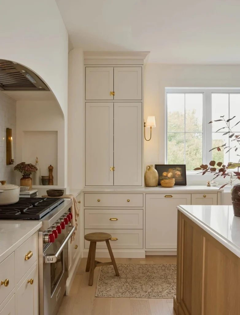Classic white and natural wood kitchen with tall cabinet, brass hardware, and terrazzo flooring