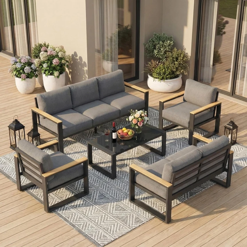 Modern outdoor patio furniture set with gray cushions, black metal frame, and wood accents on wooden deck with planters