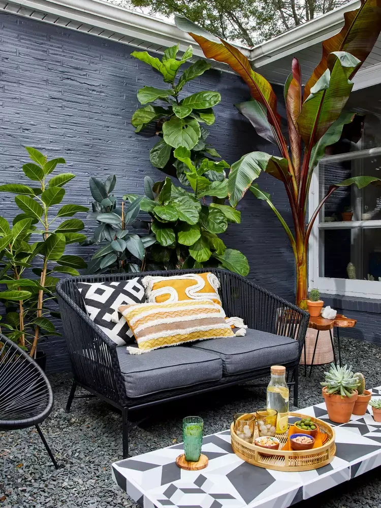 Cozy small patio with black loveseat, tropical plants, geometric tile coffee table, and dark painted brick wall