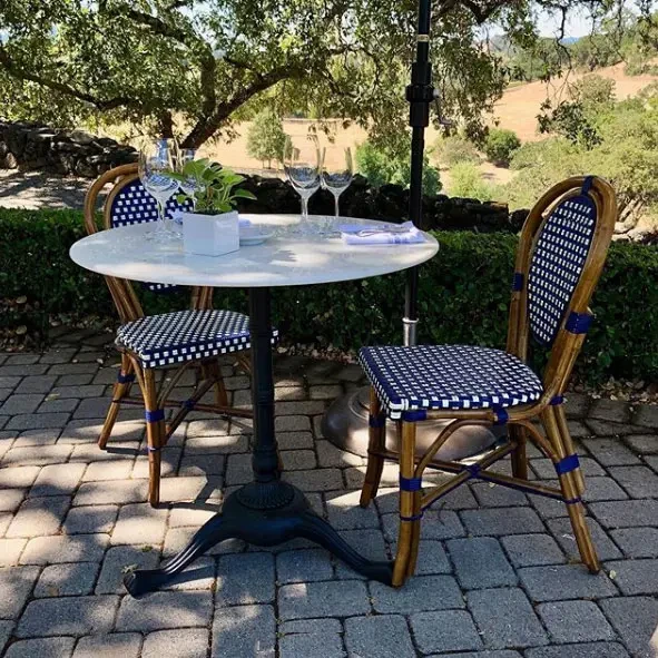 Bistro table with marble top and two French-style wicker chairs on paver patio overlooking garden