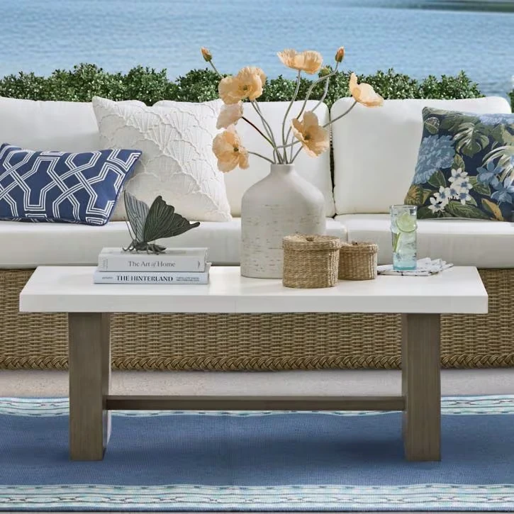 Blue patterned outdoor rug under white coffee table with coastal decor and wicker seating by waterfront patio
