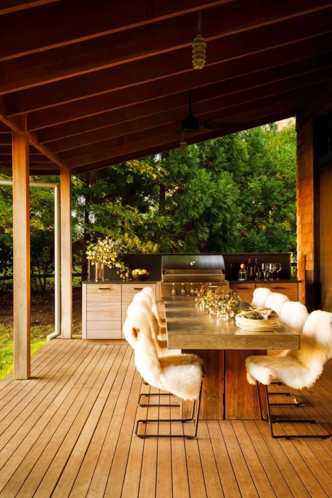 Covered wooden deck with built-in outdoor kitchen, stainless steel grill, concrete countertop, and fur-covered bar stools