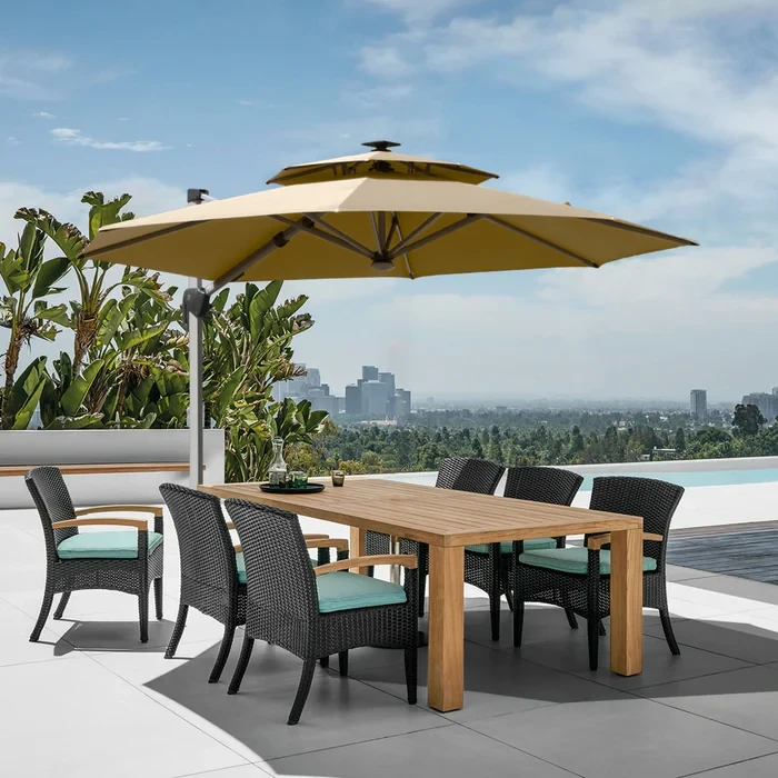Rooftop dining area with wooden table, wicker chairs, beige umbrella, and infinity pool overlooking city skyline