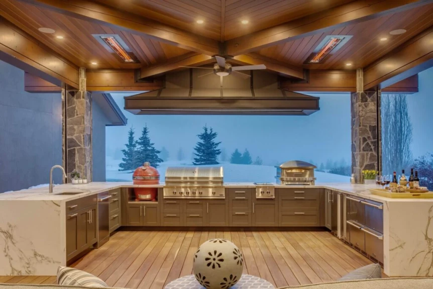 Luxury covered outdoor kitchen with wood ceiling, stone columns, built-in grill, pizza oven, and mountain view