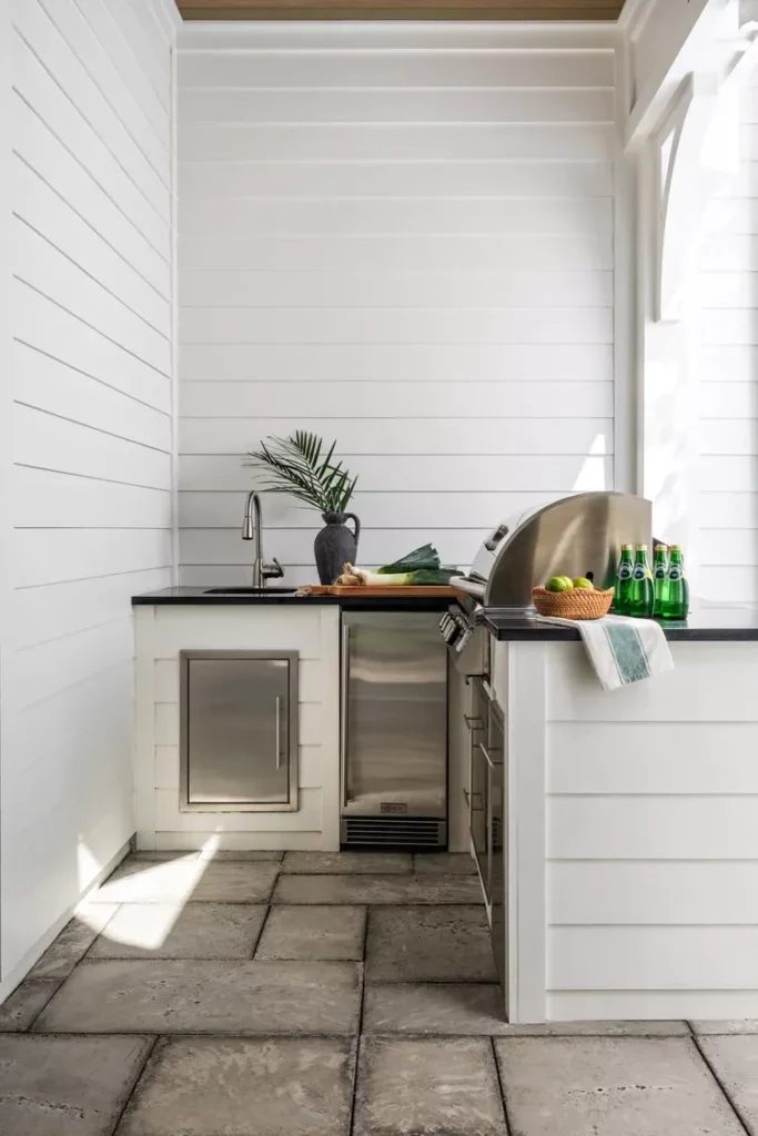 White shiplap outdoor kitchen with stainless steel grill, black countertops, and concrete pavers flooring