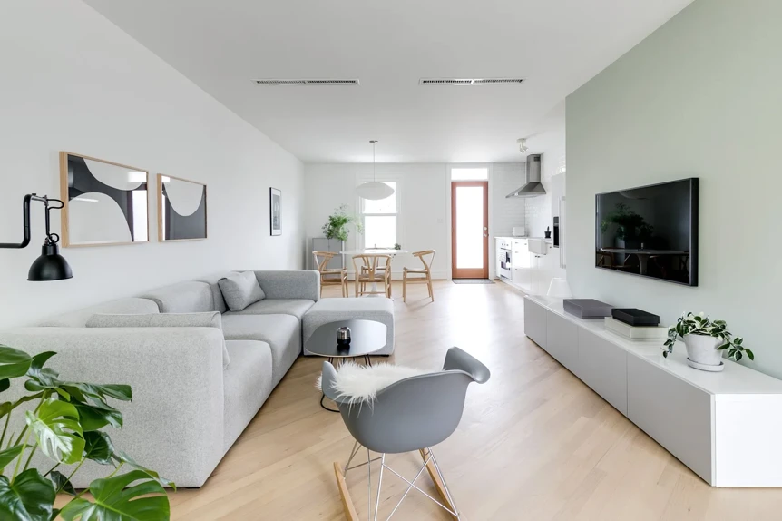Modern living room with light wood floors, gray sectional sofa, white media console, and soft green accent wall
