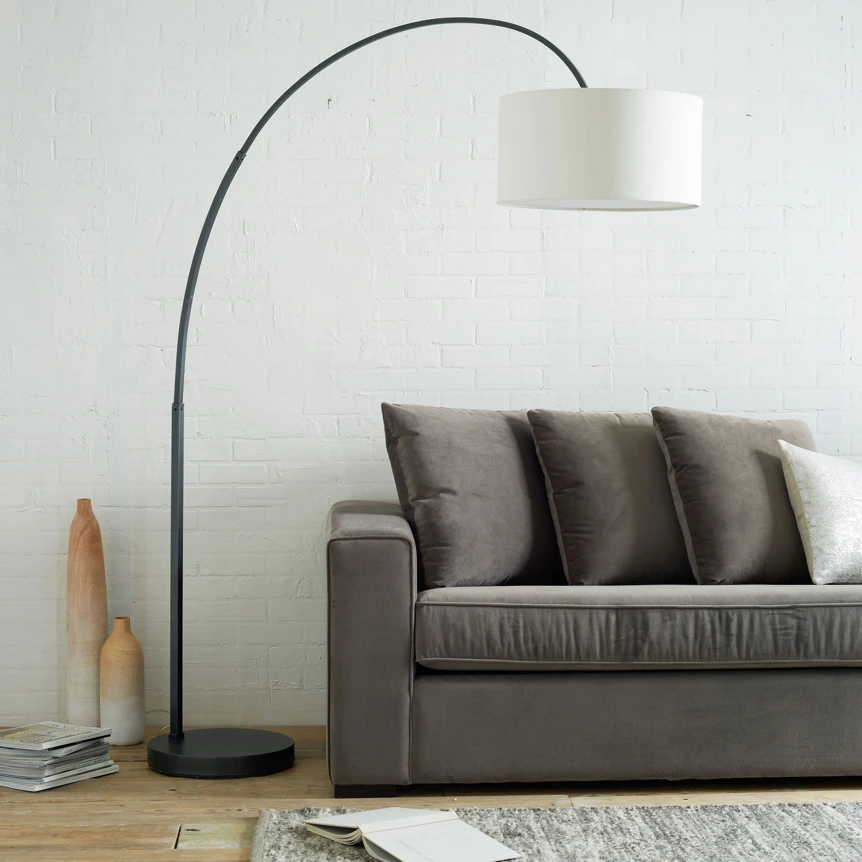Modern arc floor lamp with white drum shade beside gray sofa in contemporary living room